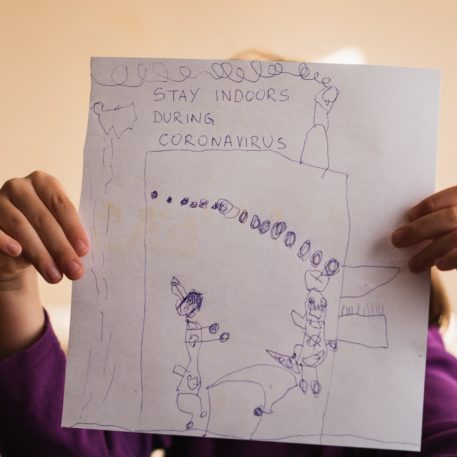 Little girl holding drawing with message to stay indoors during coronavirus