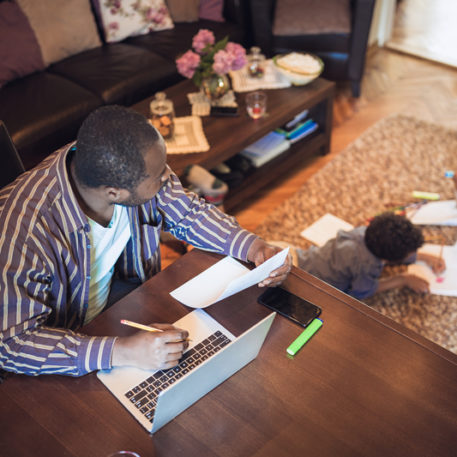 father working on the computer while looking at his son doing work on the floor