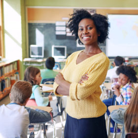 African American, female teacher posing at the back of her classroom