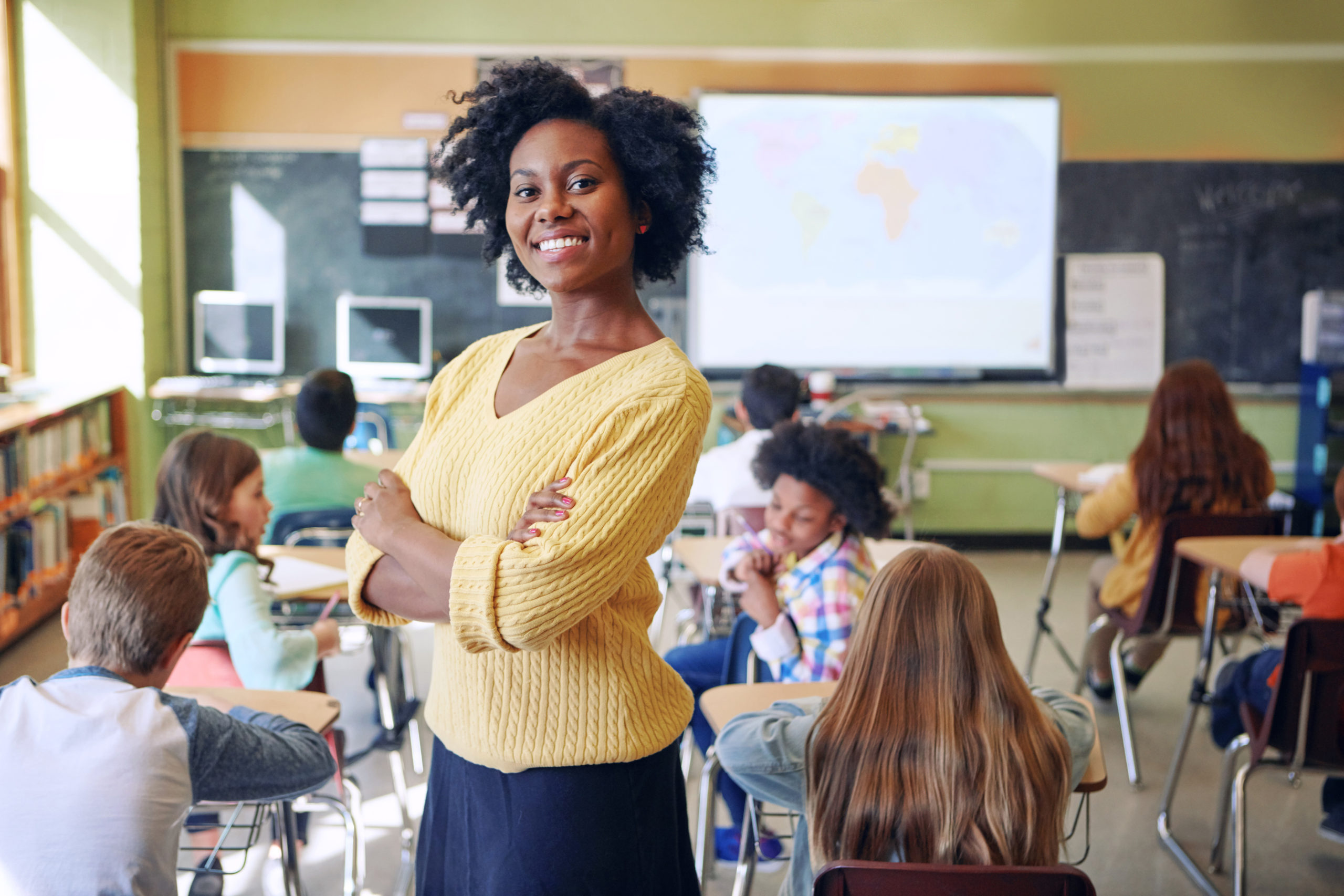 African American, female teacher posing at the back of her classroom