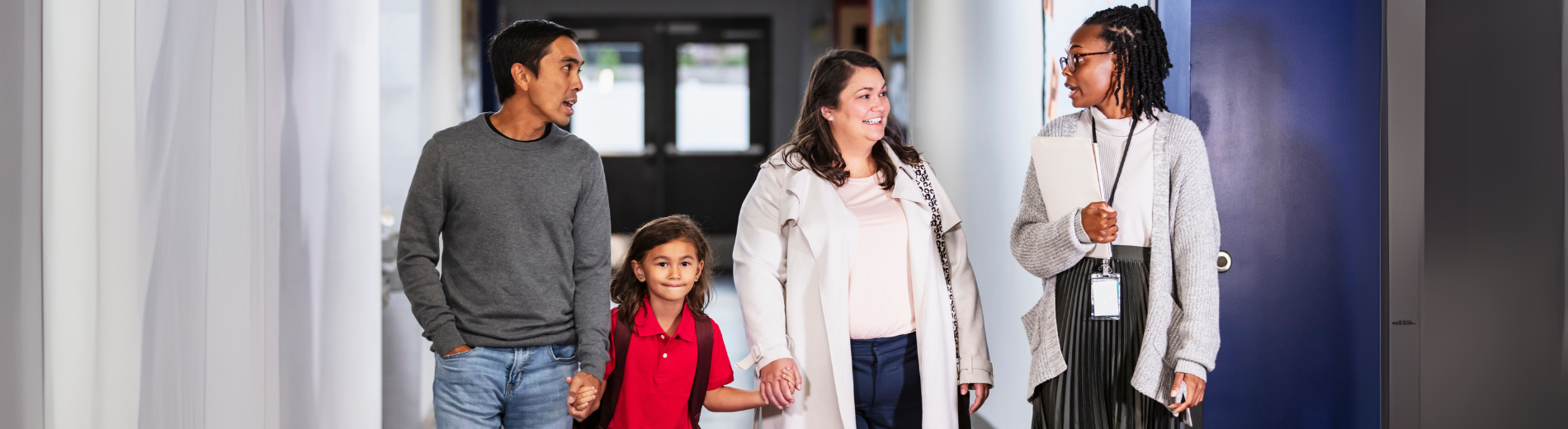 A mother and father with their daughter in the hallway a school with the teacher.